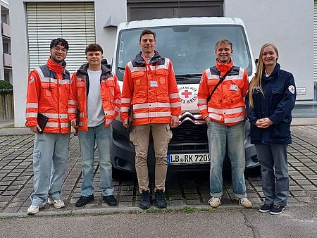 Fünf Personen in DRK-Jacken stehen vor einem Auto mit einem Rotkreuz-Logo